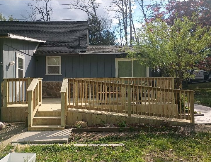 Wooden ramp and stairs leading to a house entrance with dark siding and a small tree in the yard