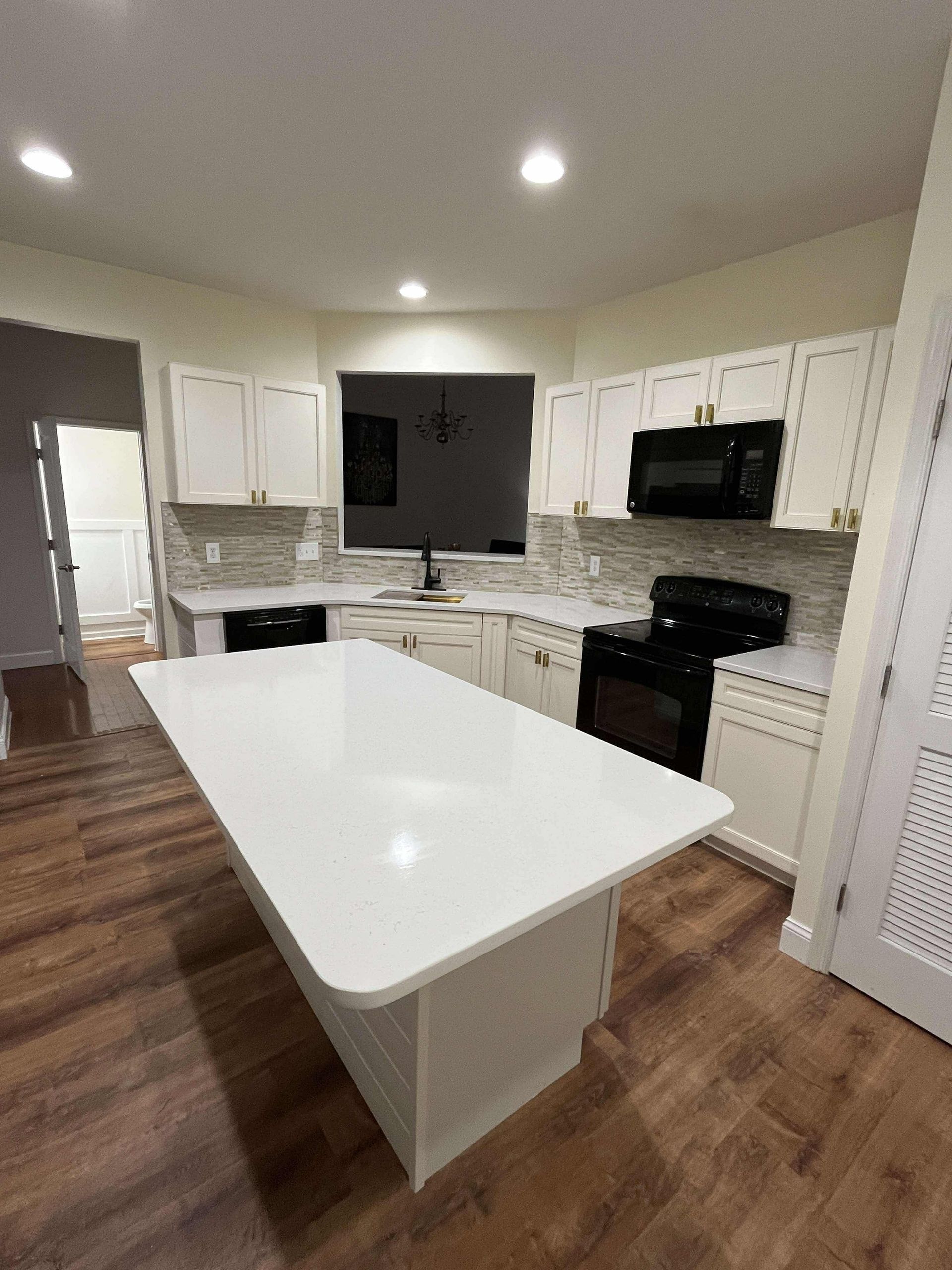Bright modern kitchen with white cabinets, black appliances, and a central island over wood flooring