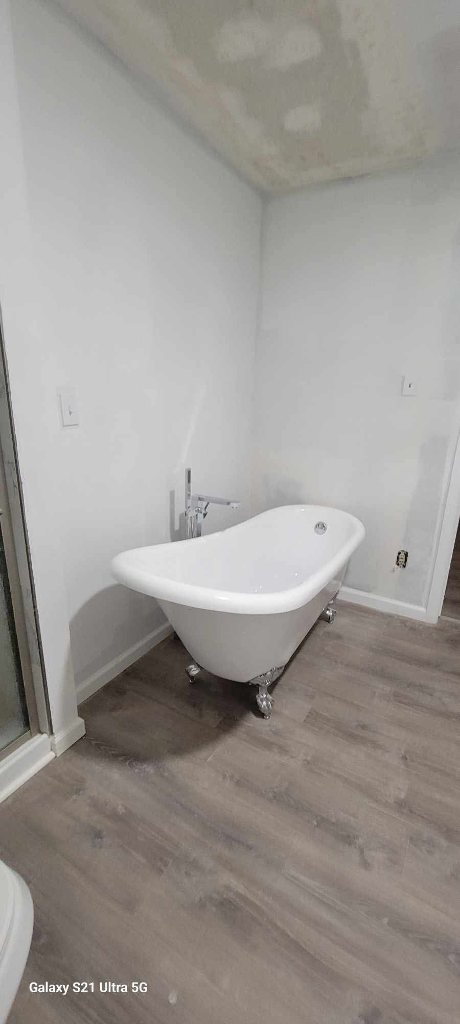 Small bathroom with a freestanding white tub, unfinished ceiling, and gray wood-look floor