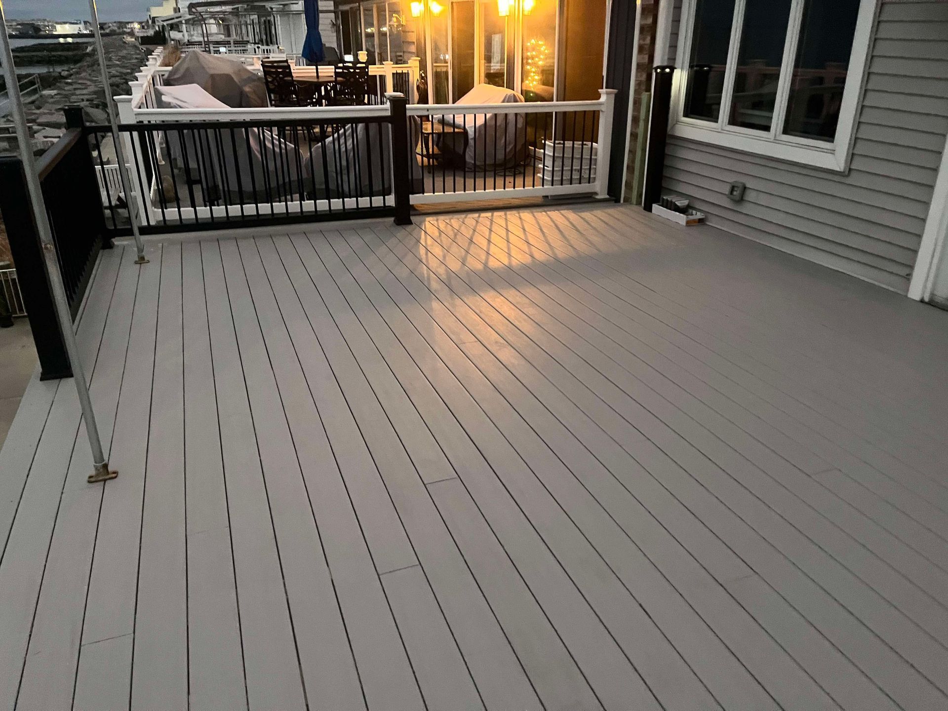 Empty gray deck with black railing, overlooking a marina at sunset.