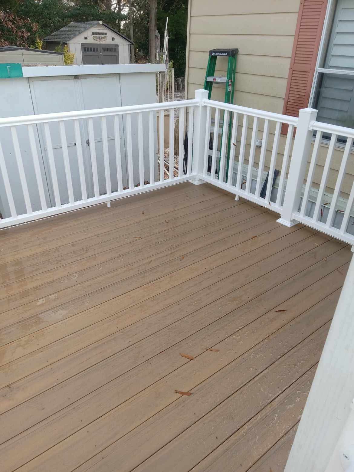 White-railed wooden deck with tan floorboards beside a house and backyard gate
