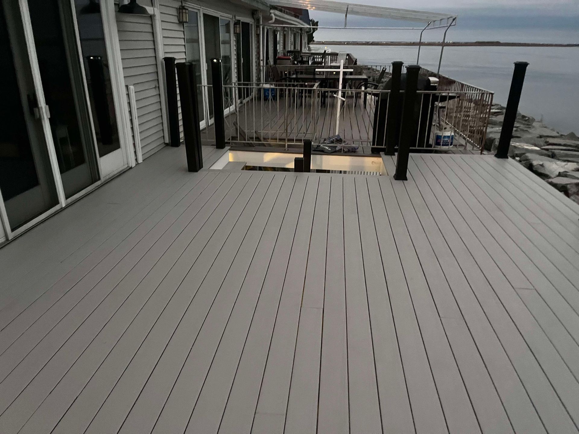 Snowy deck beside house, overlooking a cold waterfront with railings and docks.