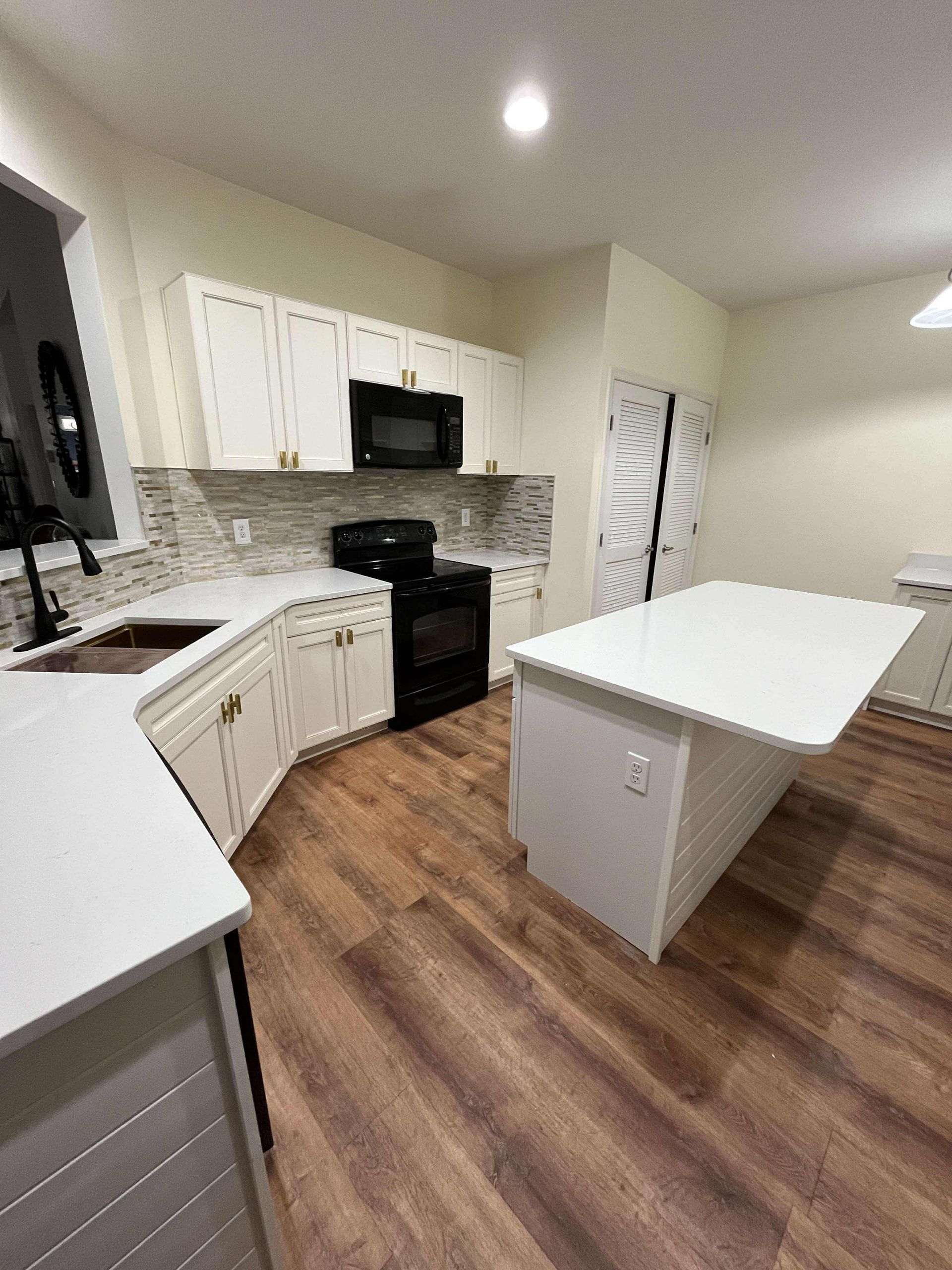 Bright kitchen with white cabinets, black appliances, tiled backsplash, and a white island.