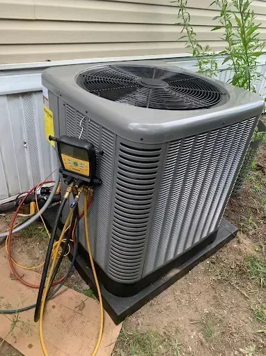 Air conditioning unit with gauges and hoses attached, outdoors, near a building.