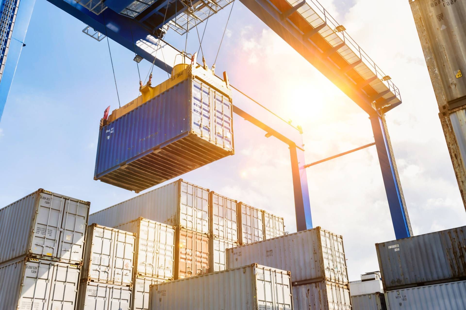 Crane lifting a shipping container above stacked containers for carrying and forwarding.