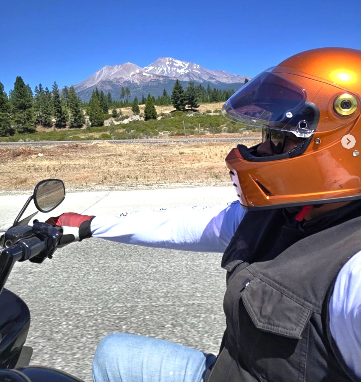 Motorcyclist in a copper helmet rides past a snowy mountain on a sunny day