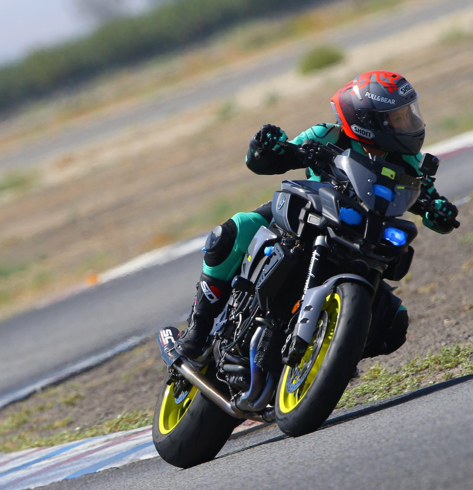 Motorcyclist in black and teal racing gear leaning into a turn on a track