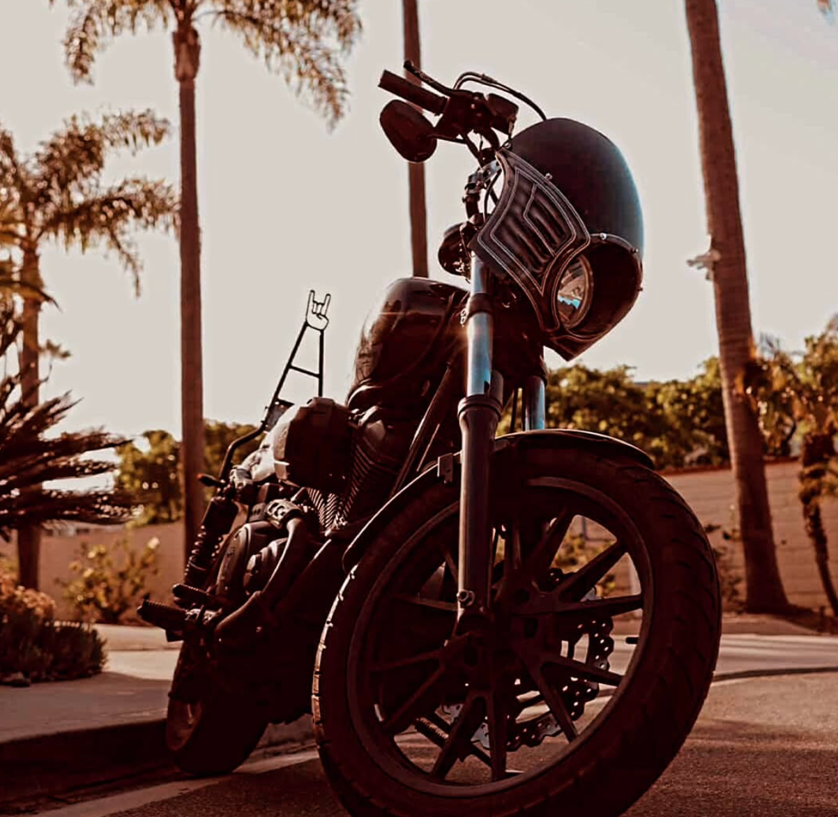 Black motorcycle parked on a palm-lined street at sunset with warm, moody lighting
