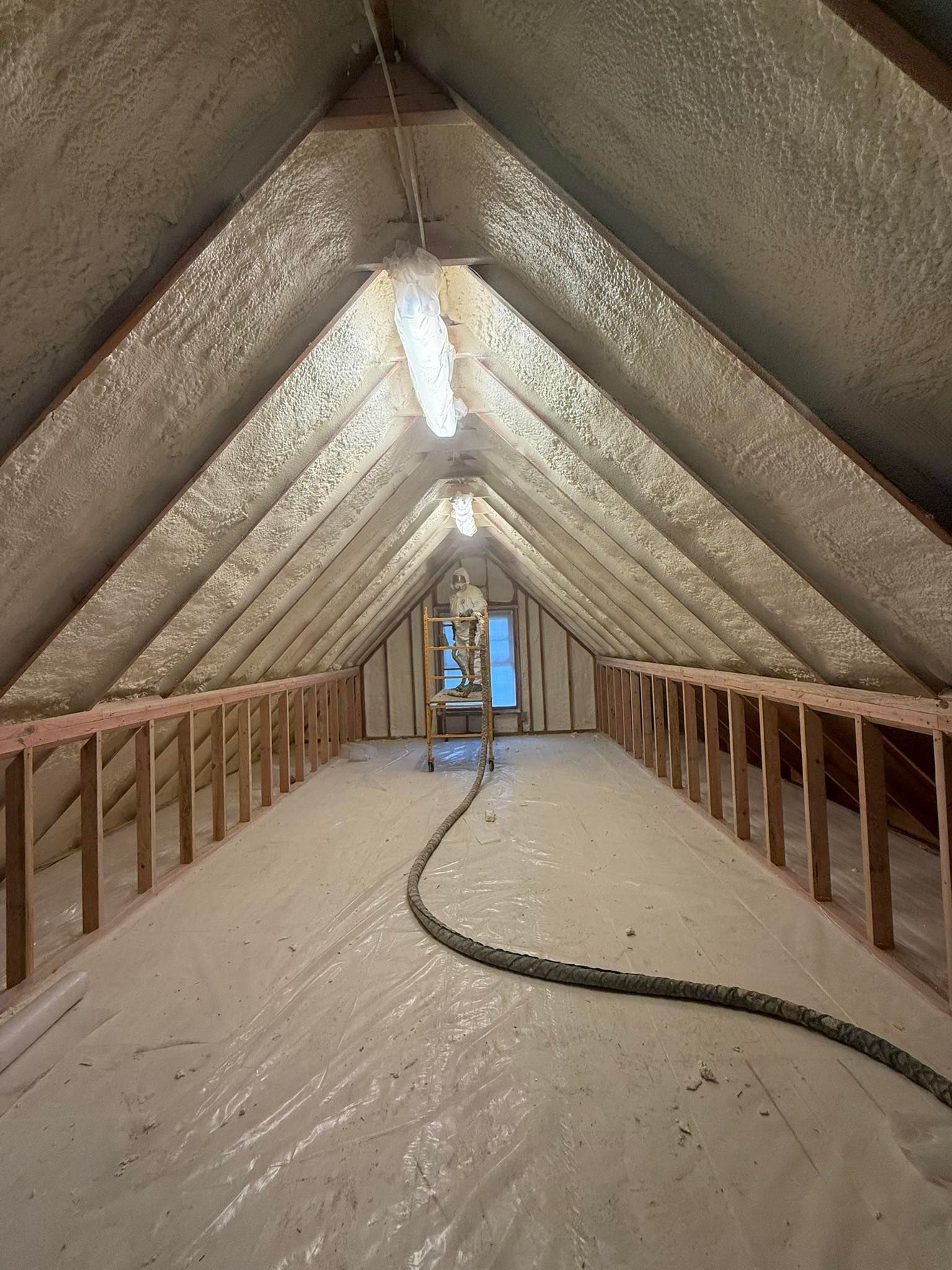 Attic under construction with insulated sloped walls, exposed framing, and a work light hanging overhead