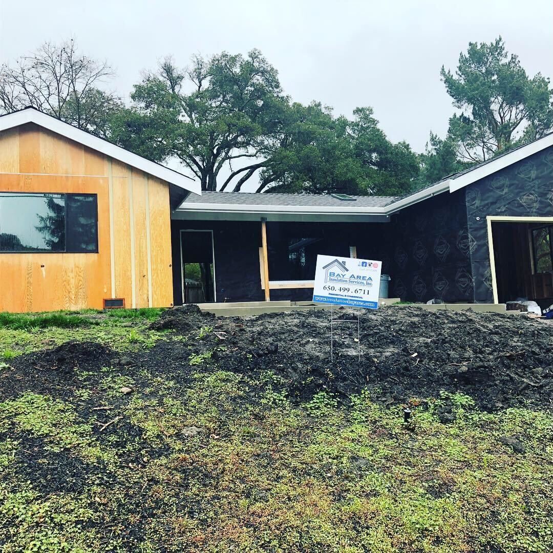Partly built house with yellow siding, dark roof, and a muddy yard under cloudy skies