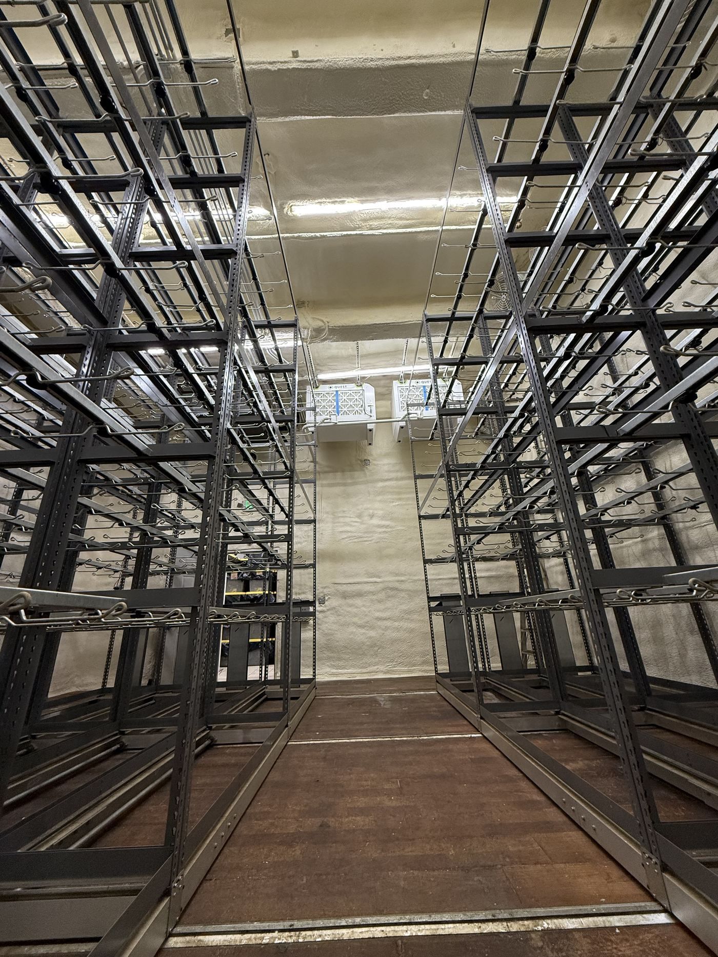 Empty warehouse aisle between tall metal storage racks and scaffolding under bright lights
