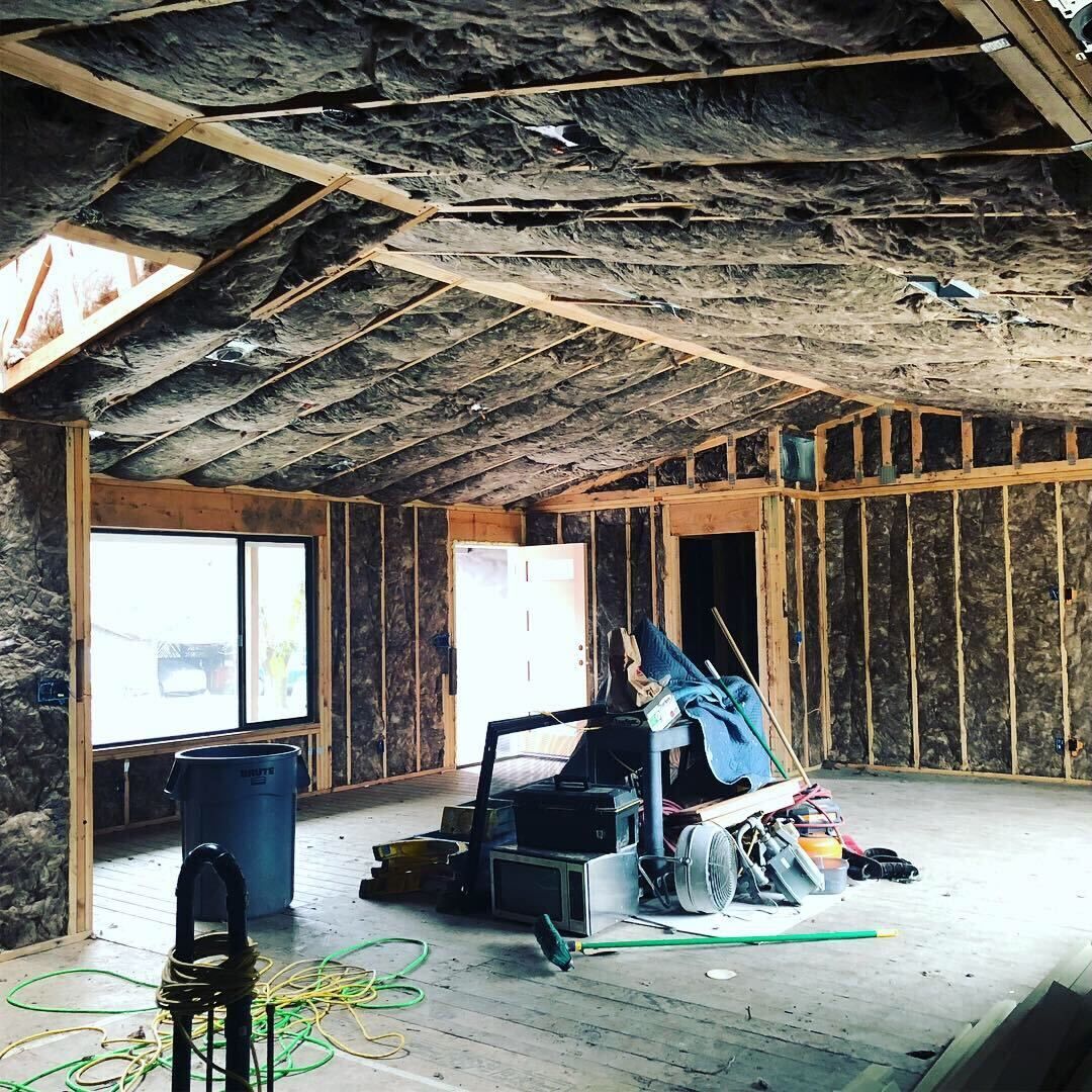 Unfinished attic interior with exposed insulation, bare studs, windows, and tools on the floor
