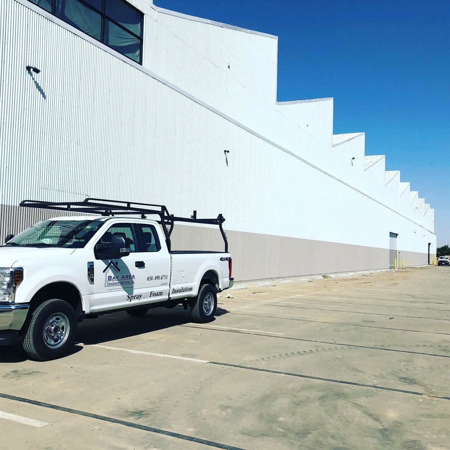 White utility truck parked beside a long white industrial building under a bright blue sky