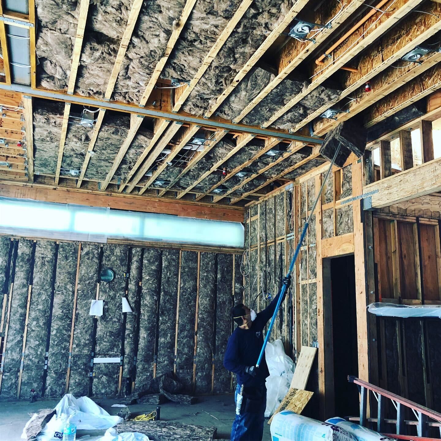 Worker insulating a partially built room with exposed wood framing and ceiling beams
