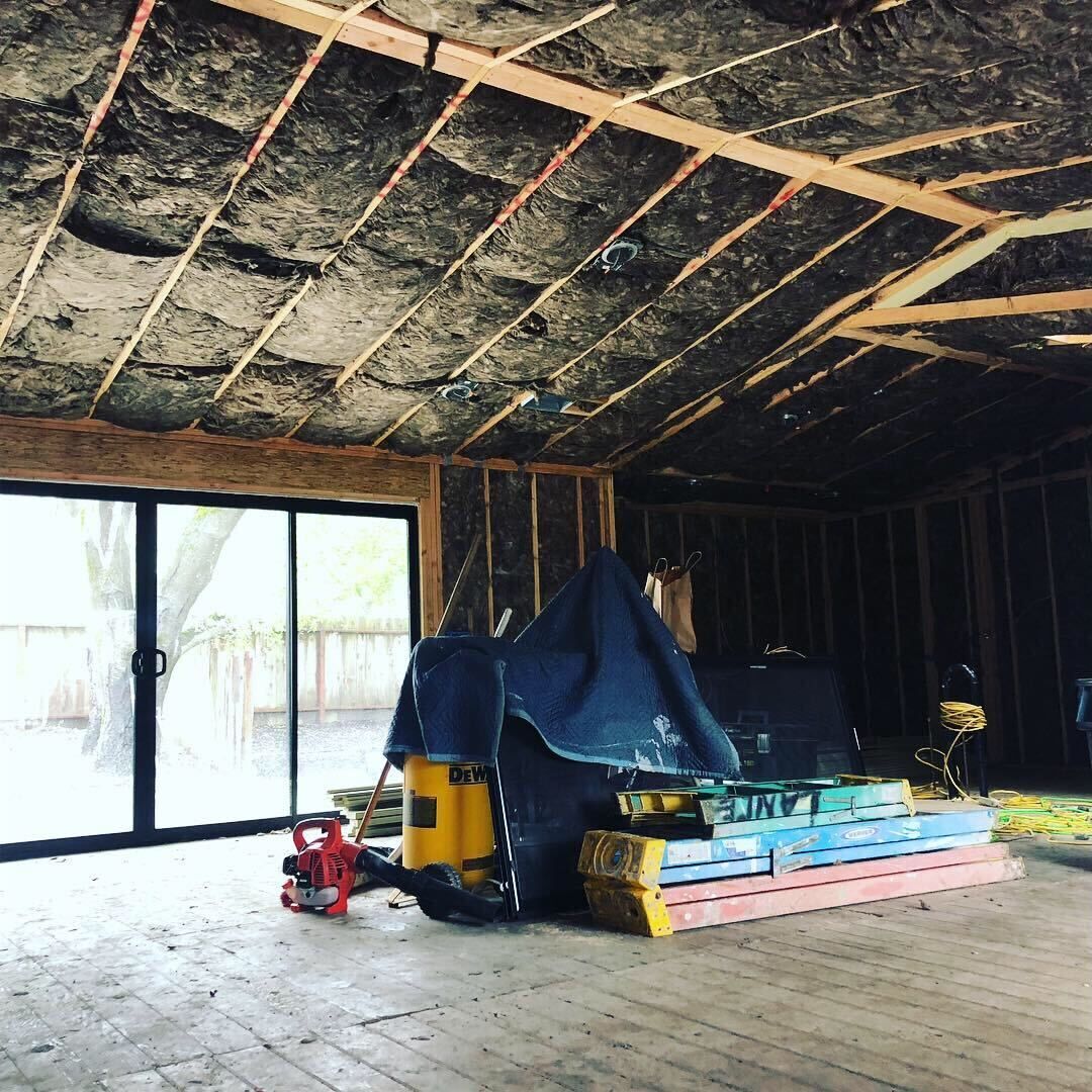 Partially renovated room with exposed insulation, sliding glass doors, and covered construction equipment on the floor