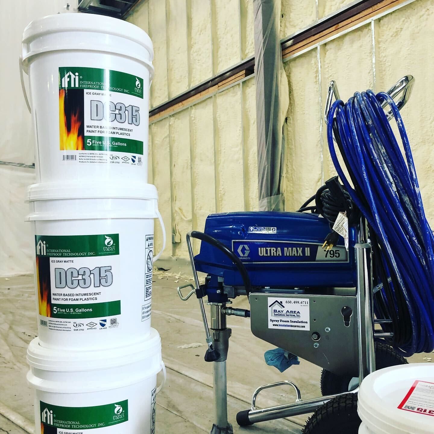 Buckets and coiled blue hoses beside a blue industrial spray machine in a workshop