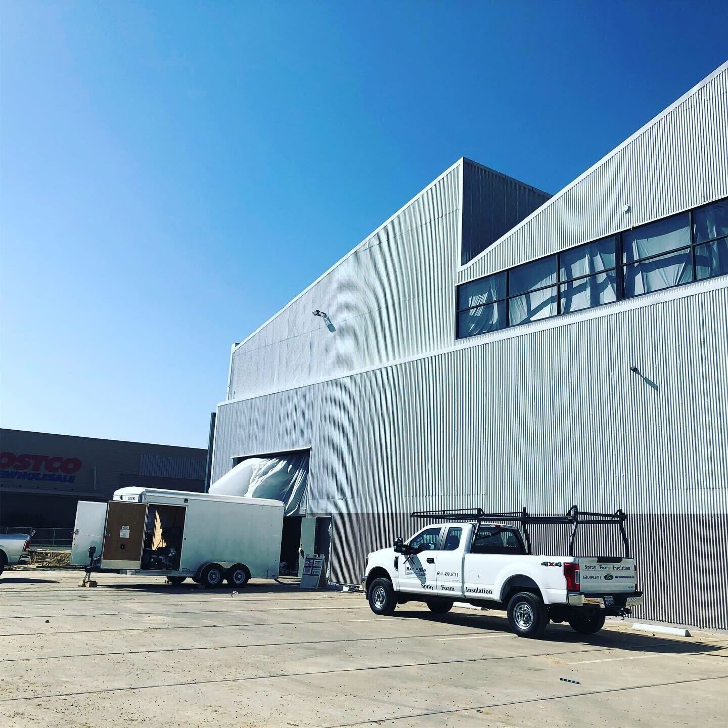 White pickup and moving truck beside a large corrugated metal warehouse under a clear blue sky