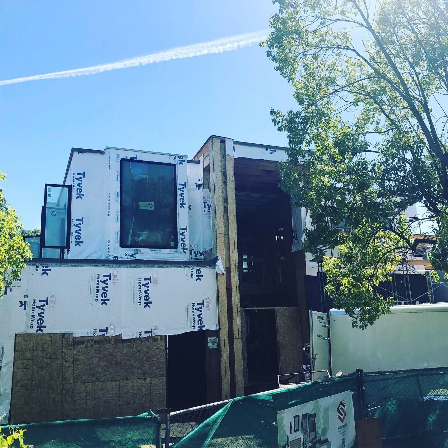 Partially built house wrapped in white housewrap, with a large open doorway under a bright blue sky