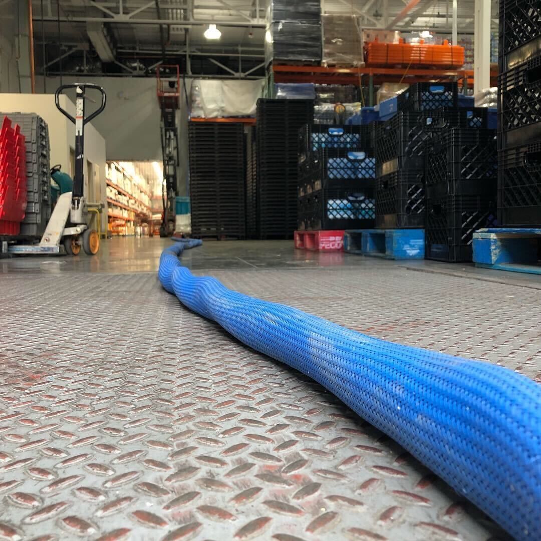 Blue hose across a warehouse floor with stacked crates and pallets in the background.