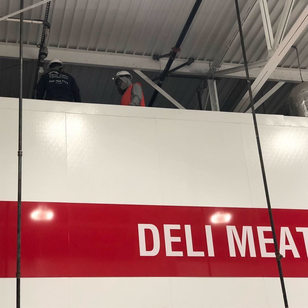 Store deli meat sign with red-and-white lettering inside a market or warehouse aisle