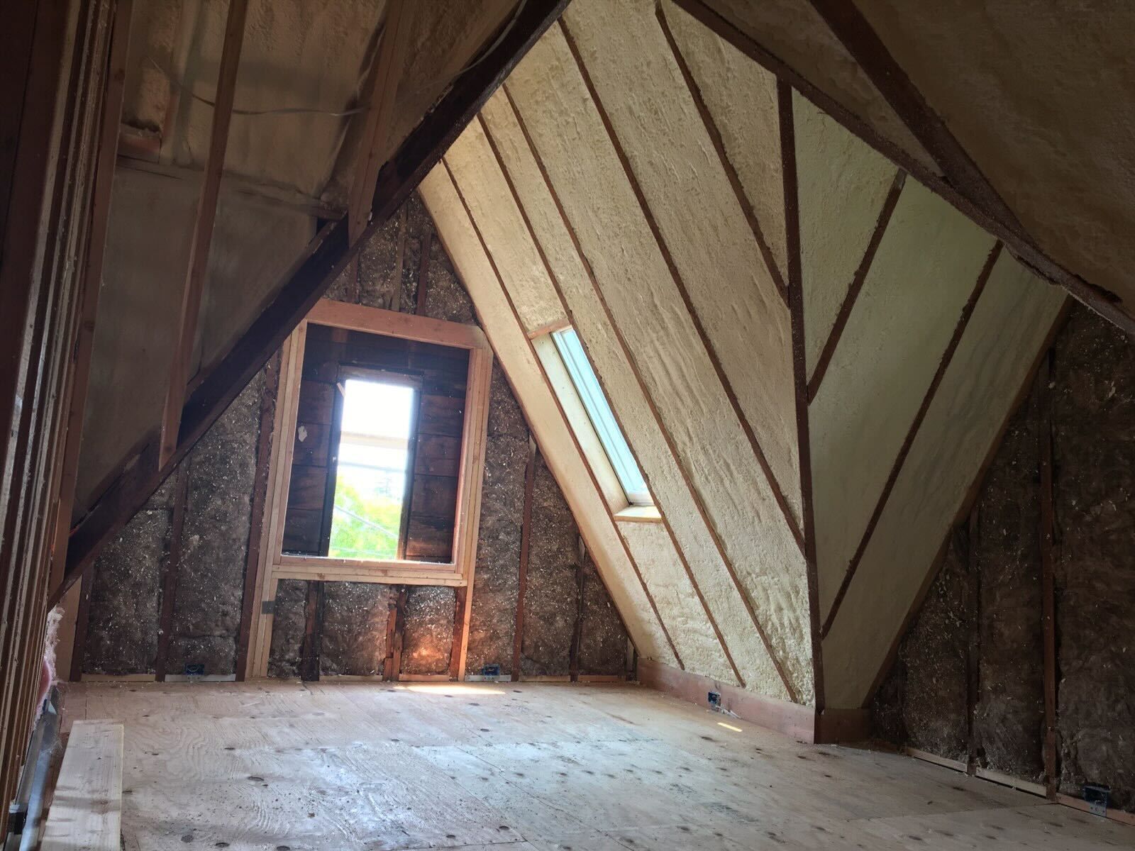 Attic room with slanted wooden walls, small window, and unfinished floor boards