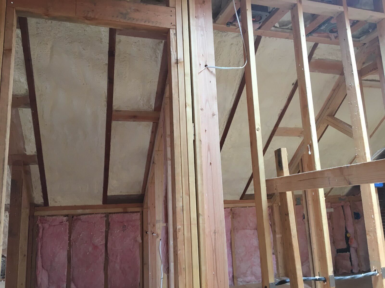 Framed interior wall under construction with exposed wood studs and pink insulation panels