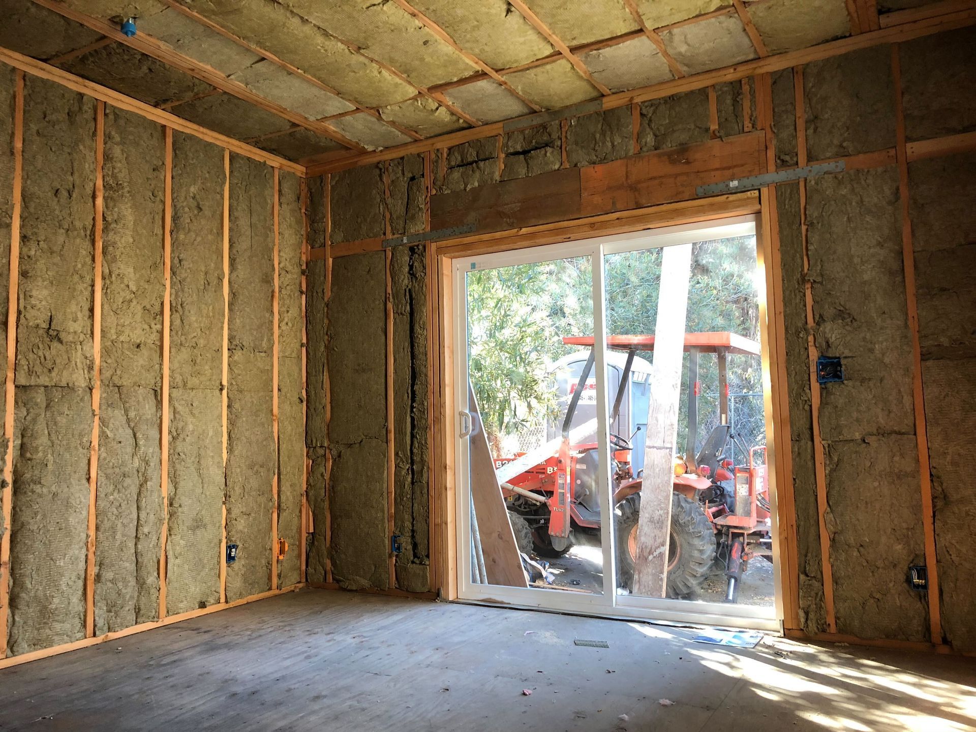 Insulated room under construction with exposed framing and a doorway opening to outdoor equipment.