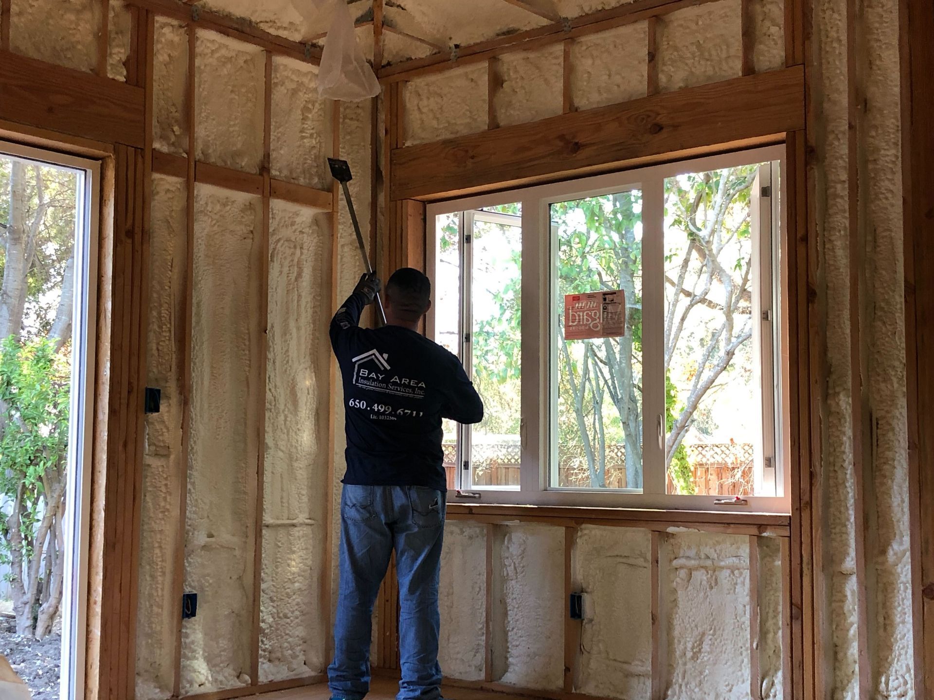Person installing insulation in a wood-framed room with large windows.