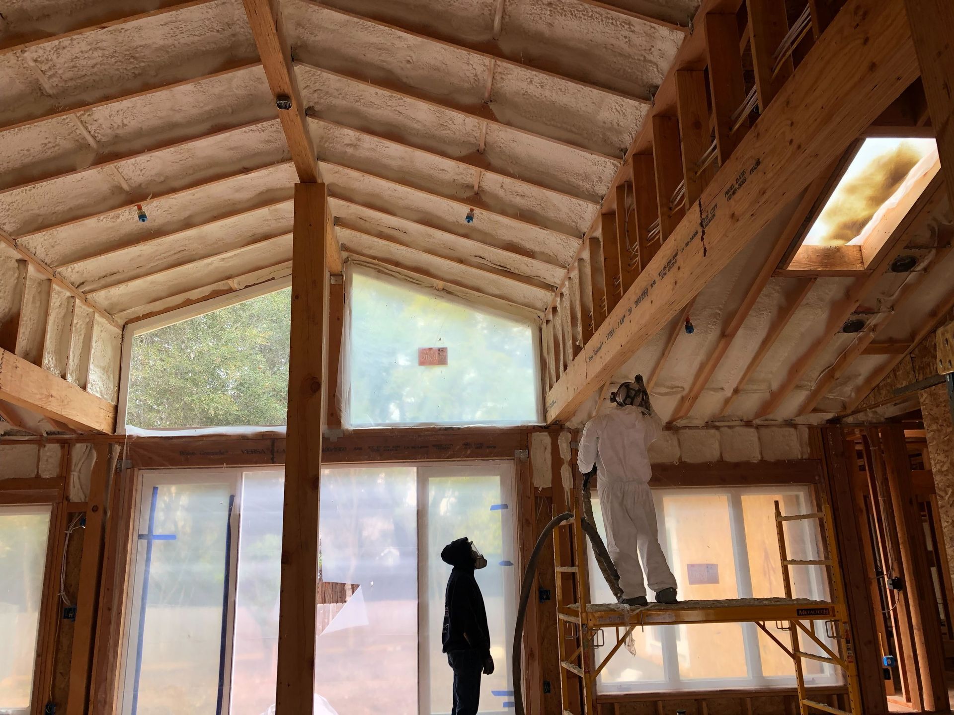 Interior of a wood-framed cabin under construction with exposed beams and large windows.