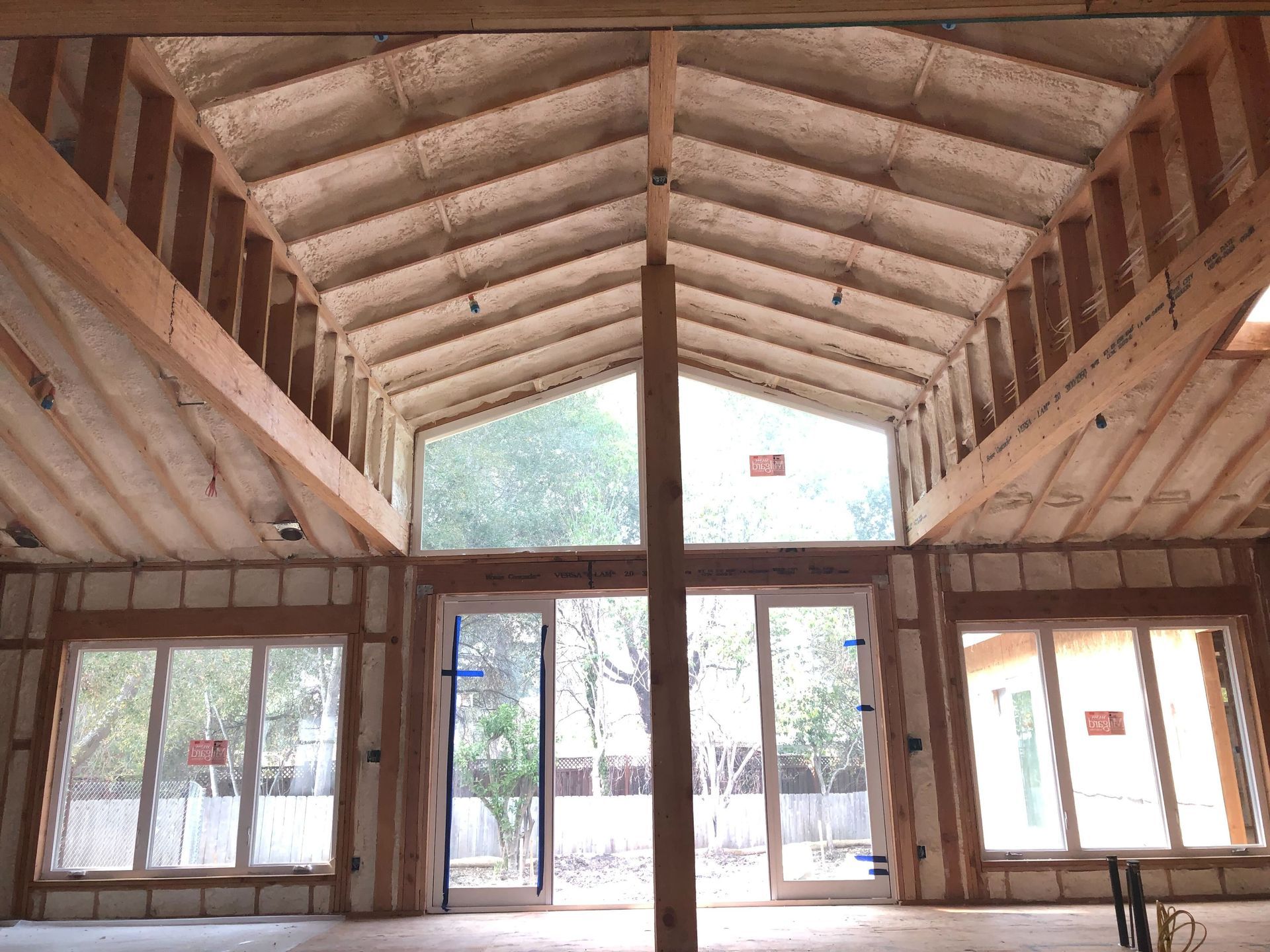 Empty wooden hall with exposed rafters, large windows, and a central doorway opening to a bright exterior.