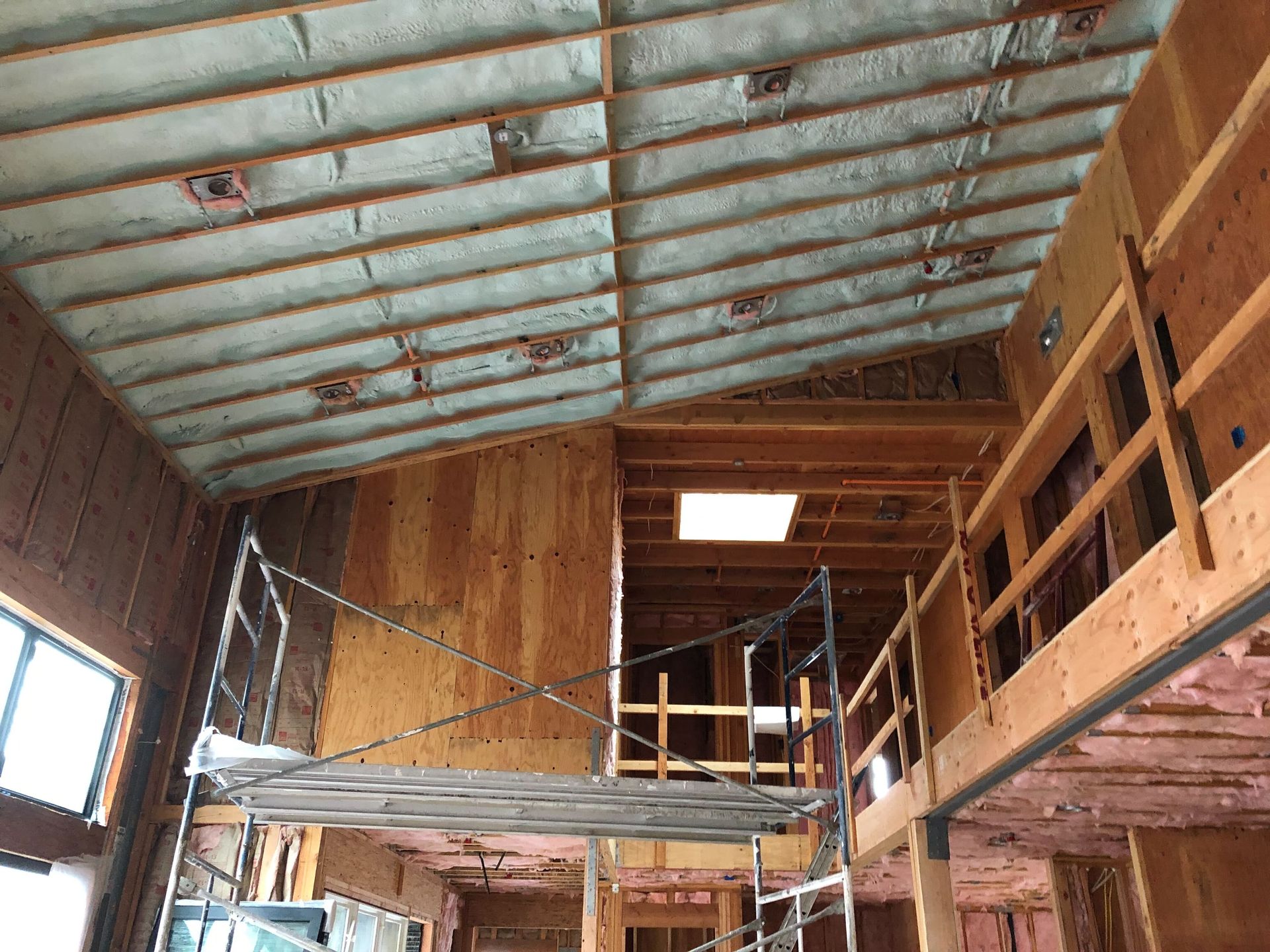Loft interior under construction with wood framing, metal roof, and scaffolding around a central opening