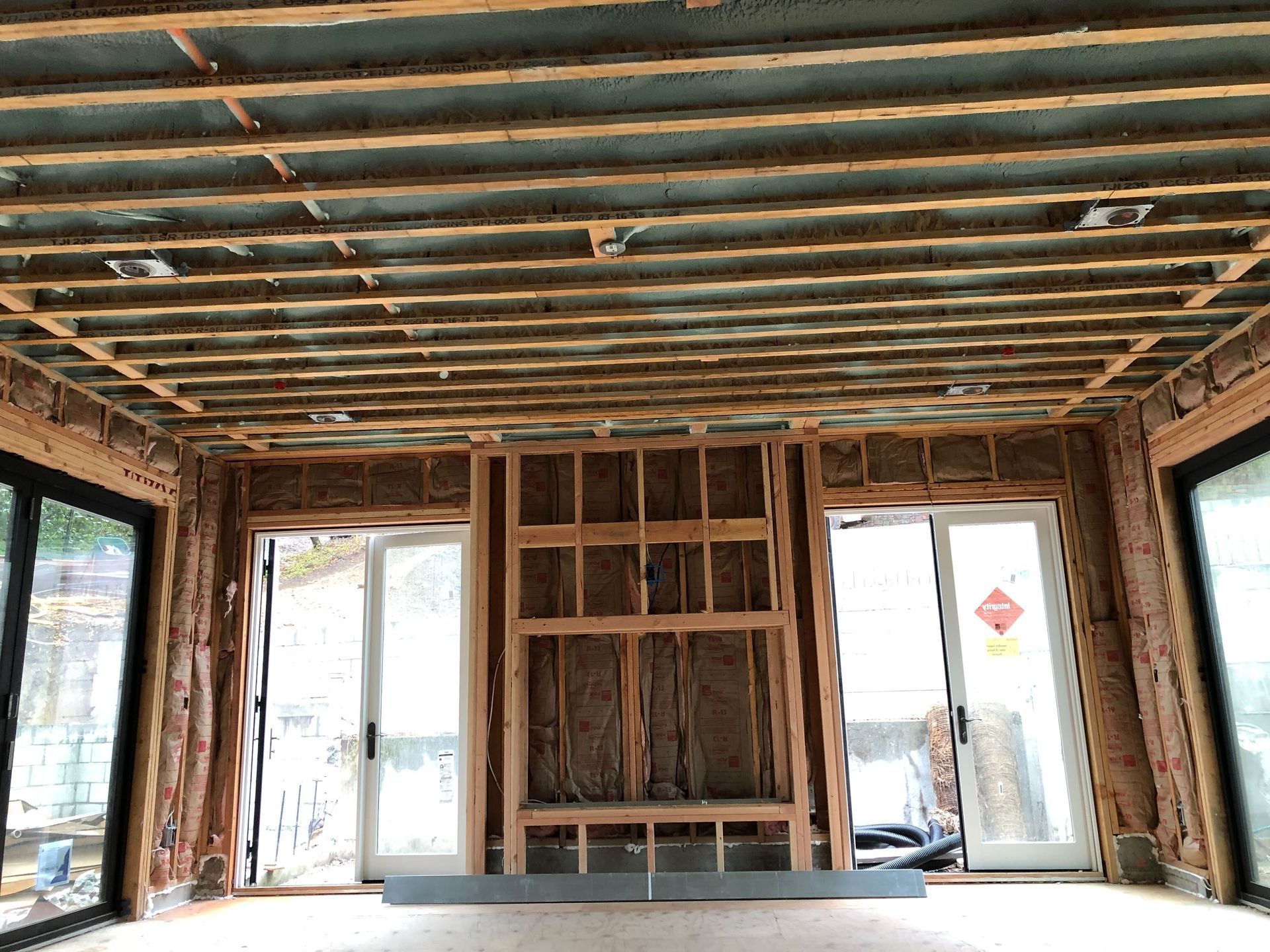 Interior of a house under renovation with exposed framing, unfinished walls, and open doorways to the outside