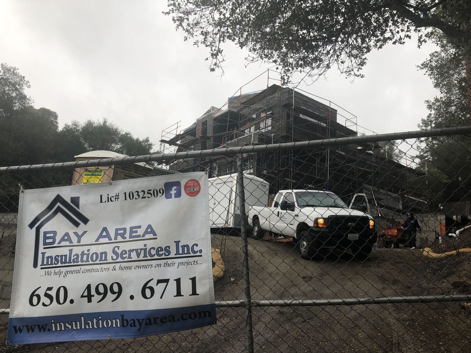 Damage restoration sign in front of a fire-damaged house with a white truck behind a chain-link fence.