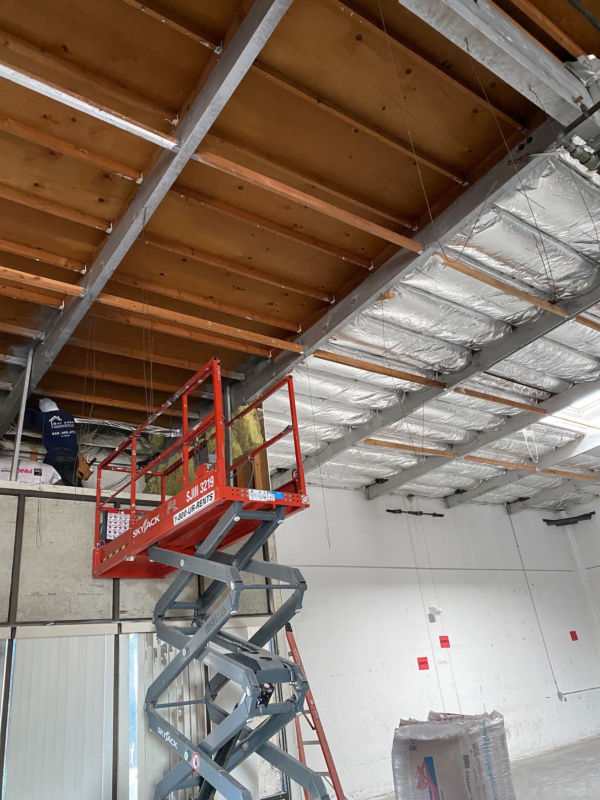 Red scissor lift with red platform inside a partially finished warehouse ceiling area