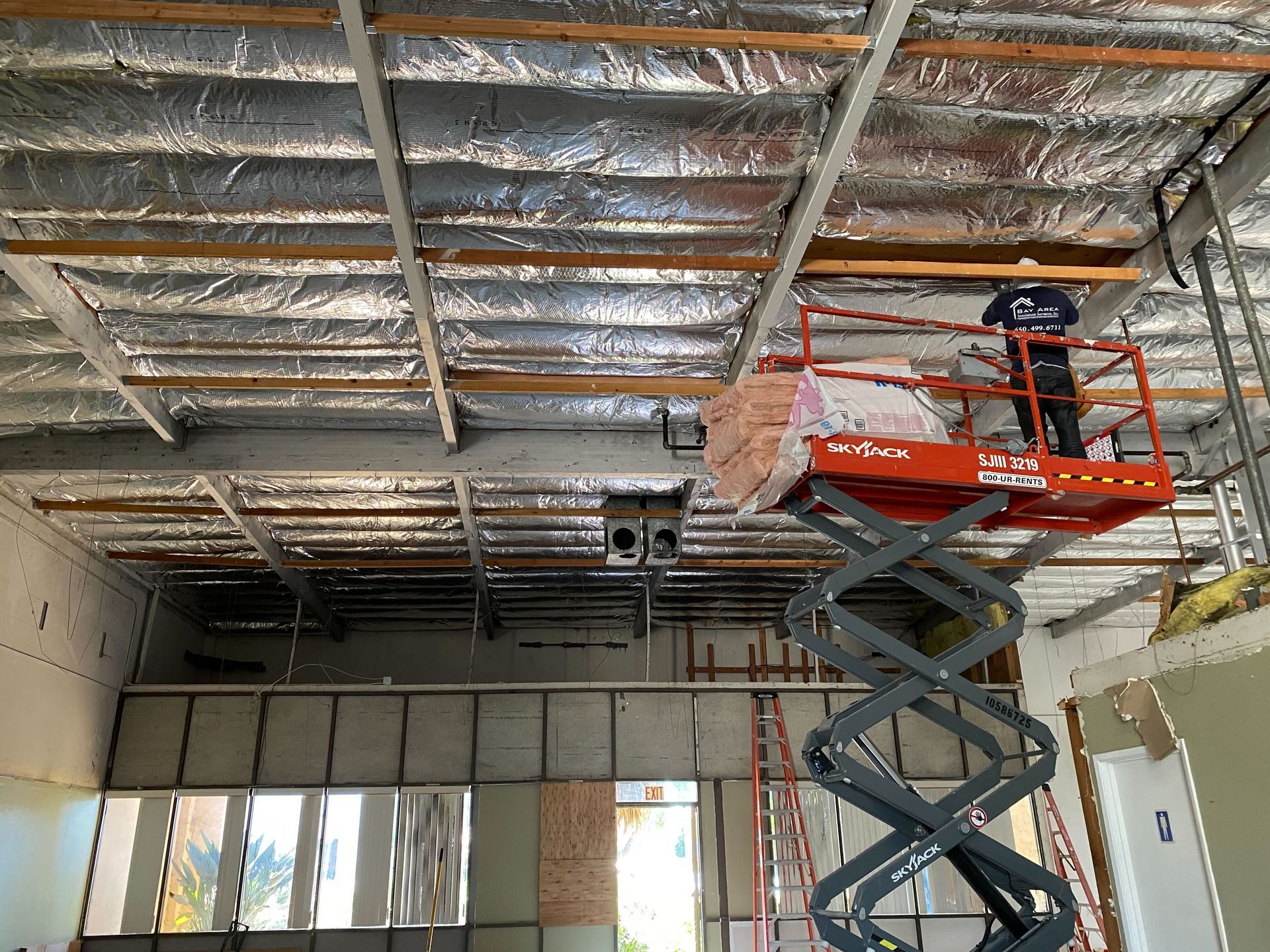 Scissor lift in a room with exposed ceiling insulation and metal framing under construction