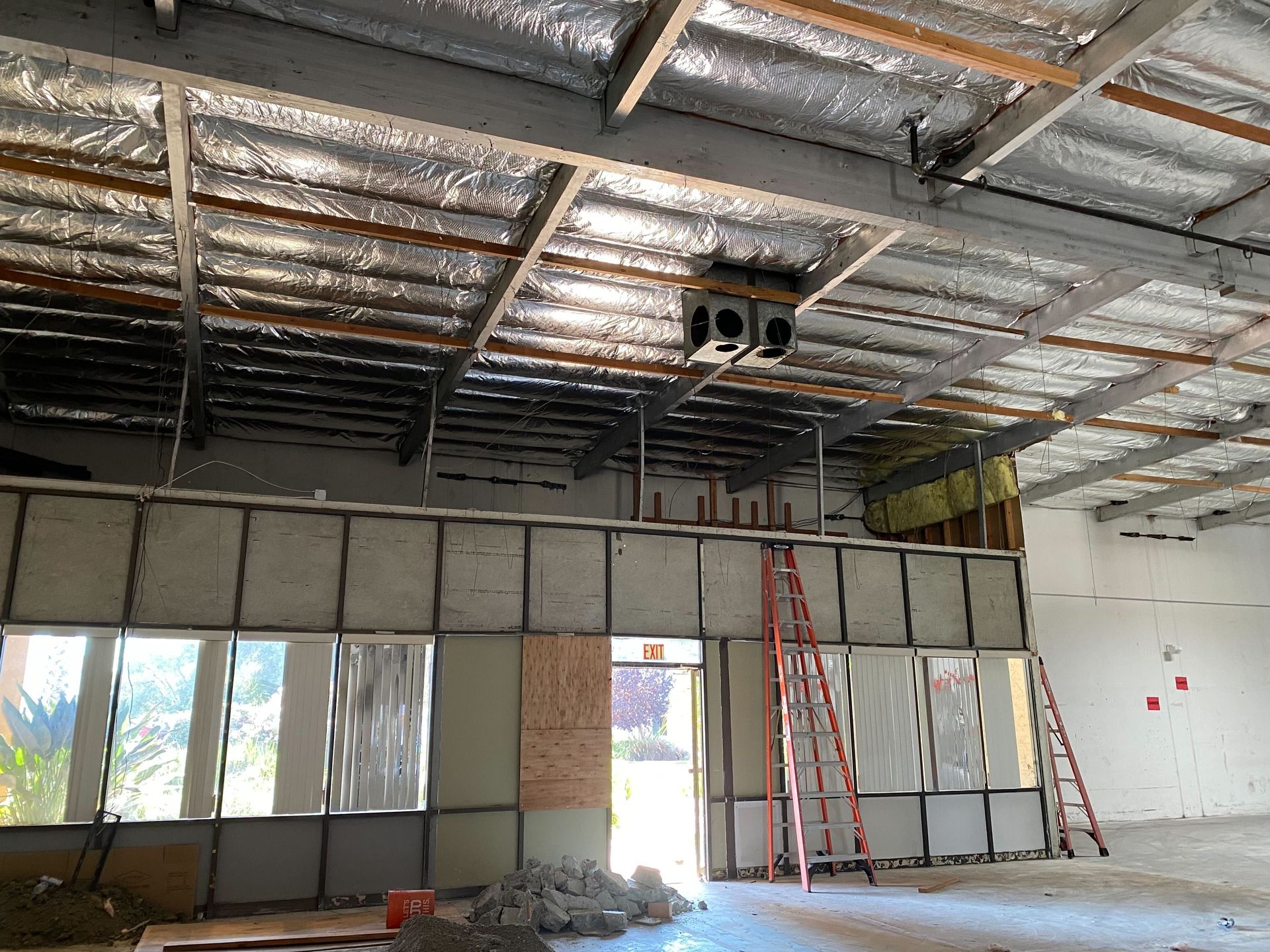 Interior under construction with exposed ceiling insulation, partition walls, windows, and a red ladder.