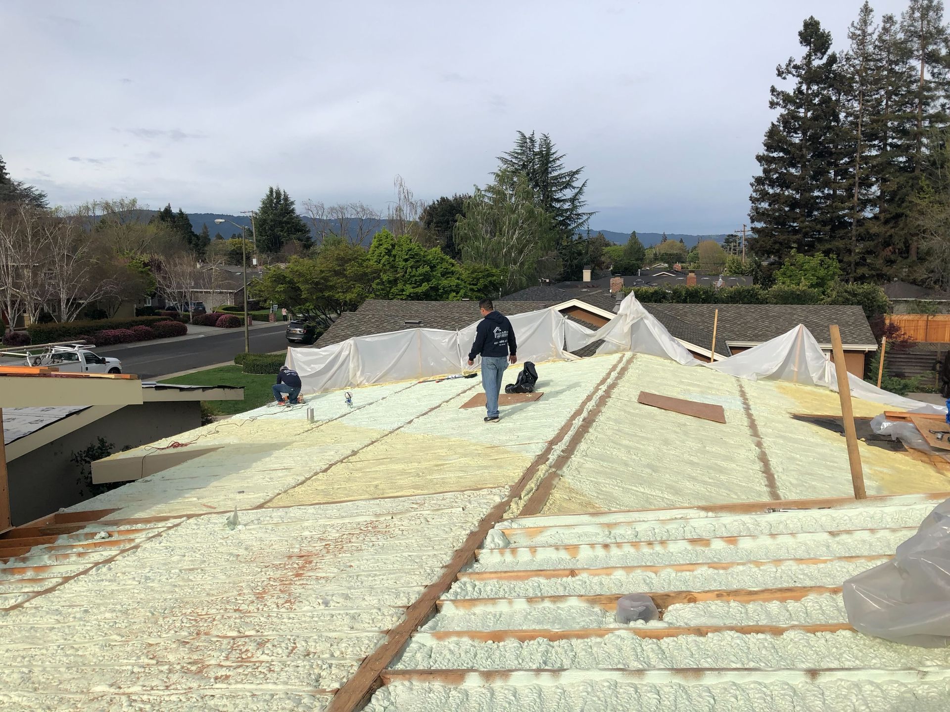 Worker on a rooftop installing insulation panels under a cloudy sky.