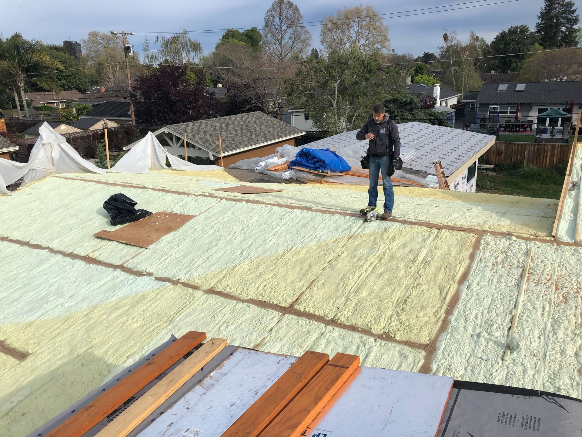 Worker standing on a roof covered with white insulation boards and tarps under a partly cloudy sky