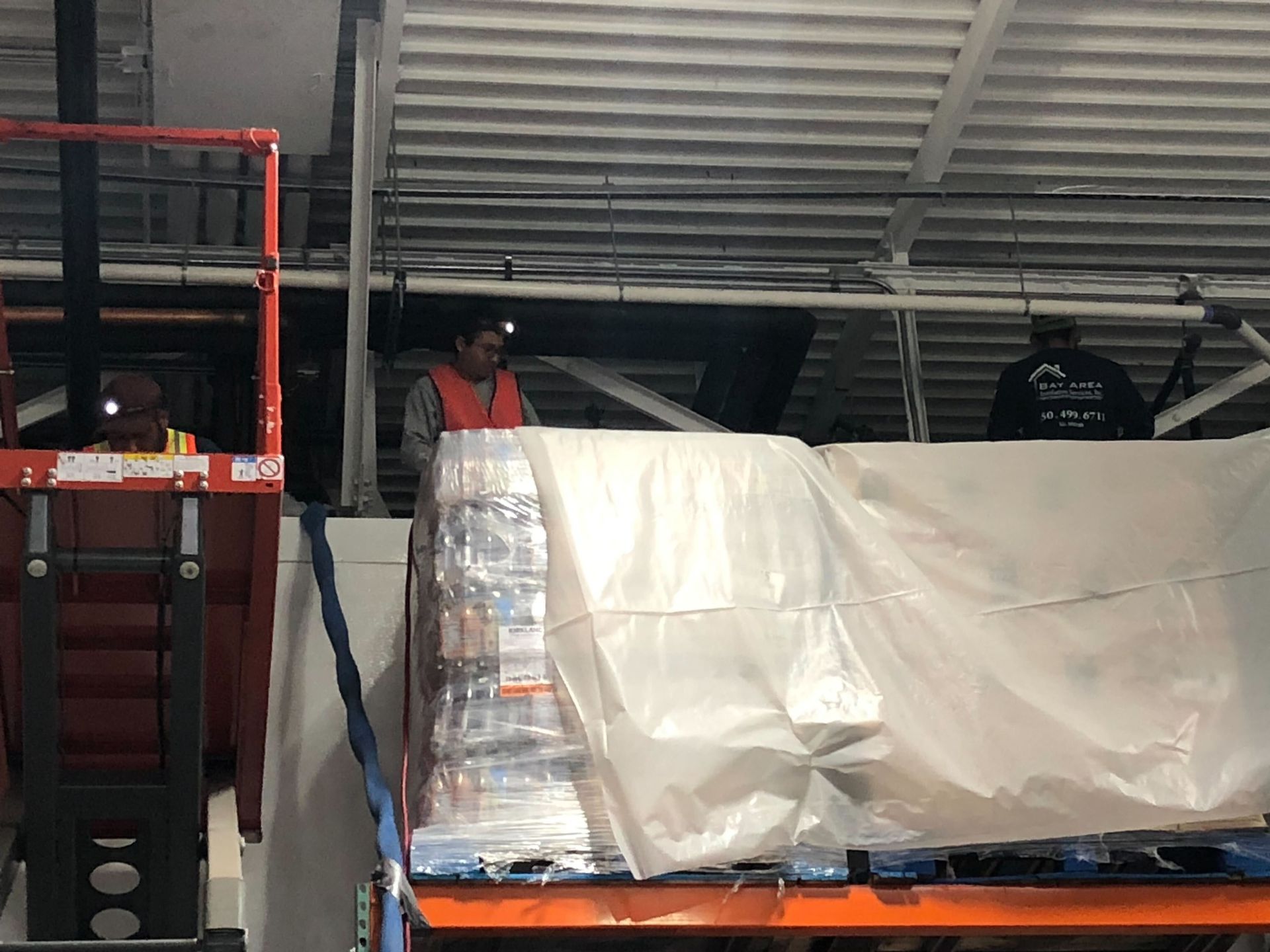 Warehouse scene with wrapped pallet cargo, forklift, and two workers near metal shelving