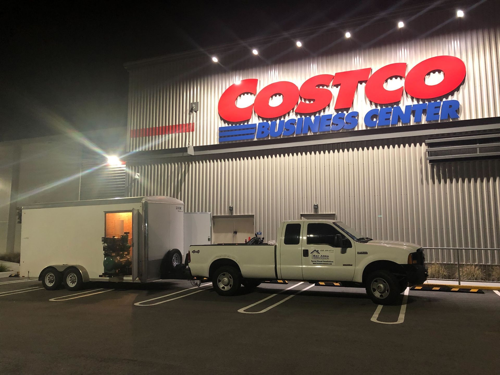 Pickup truck towing a white cargo trailer outside Costco Business Center at night
