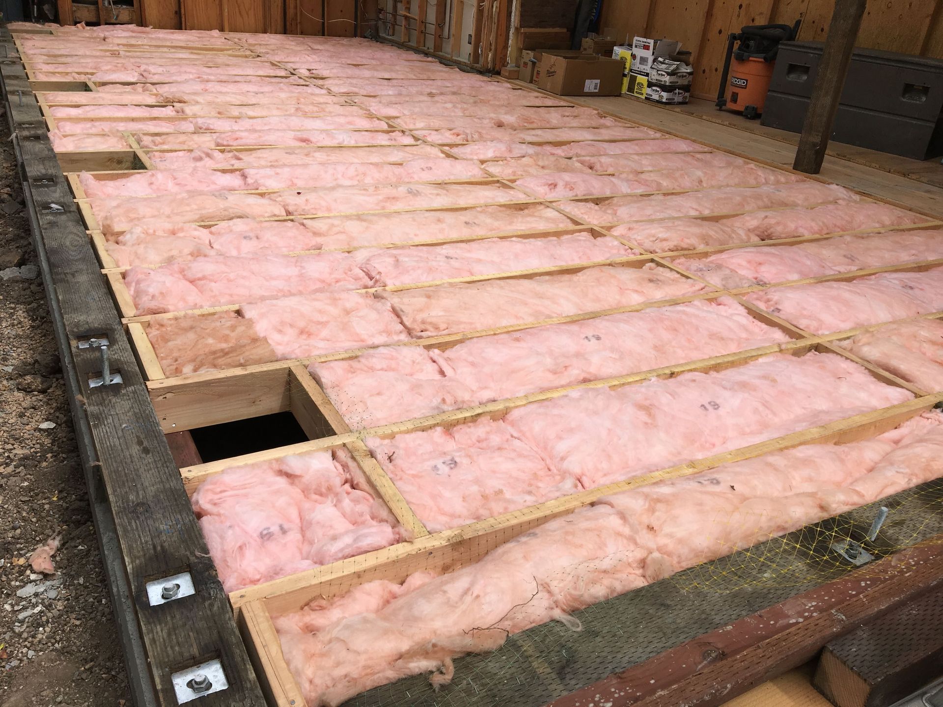 Pink insulation batts laid across a wooden floor frame in an unfinished room