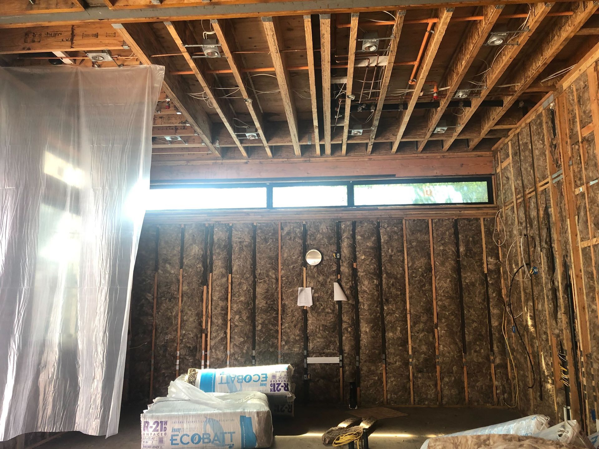 Partially renovated room with exposed ceiling joists, insulation on wall, and stacked construction materials