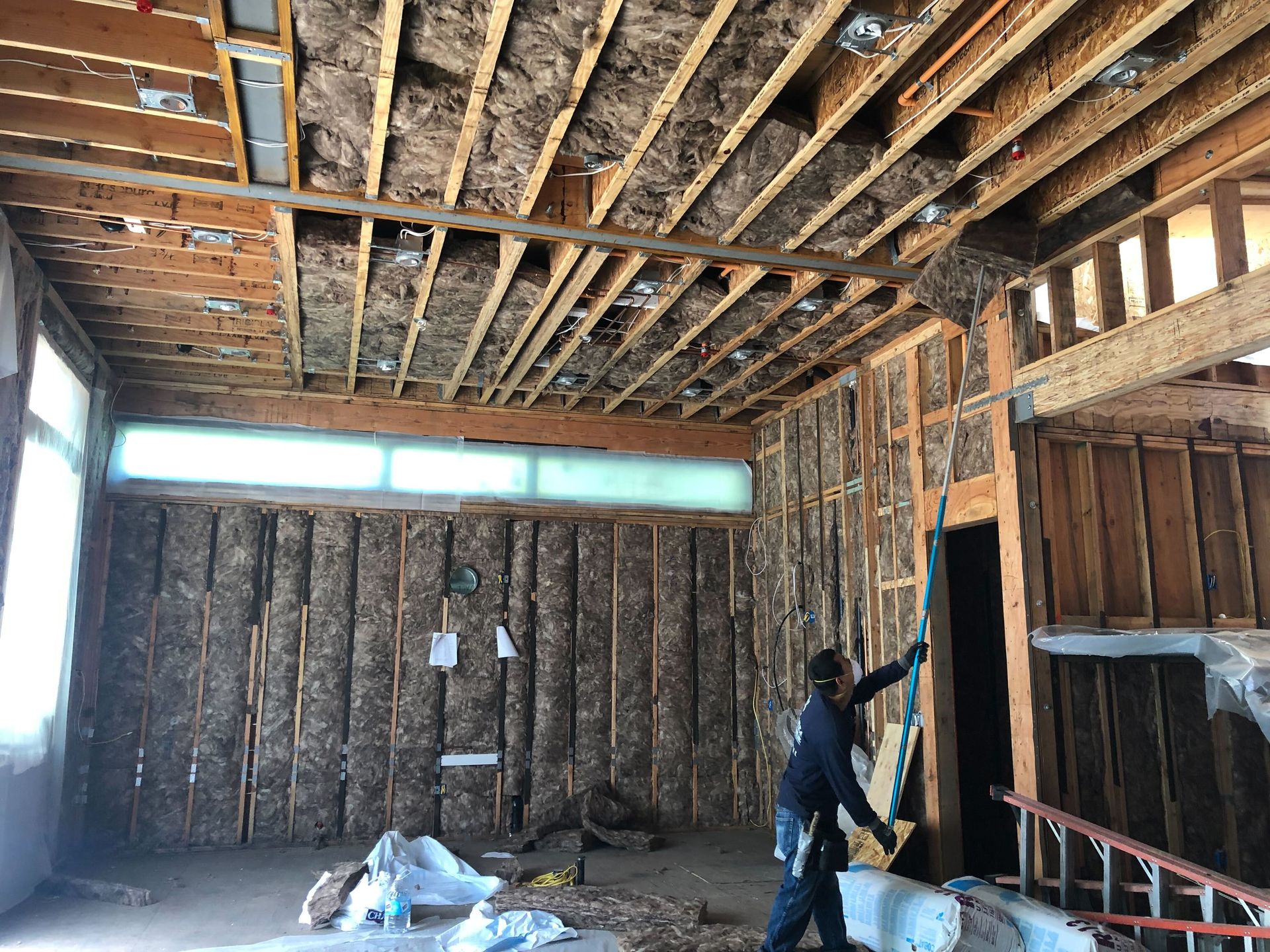 Worker inspecting exposed wooden framing in an unfinished room with a partially insulated ceiling