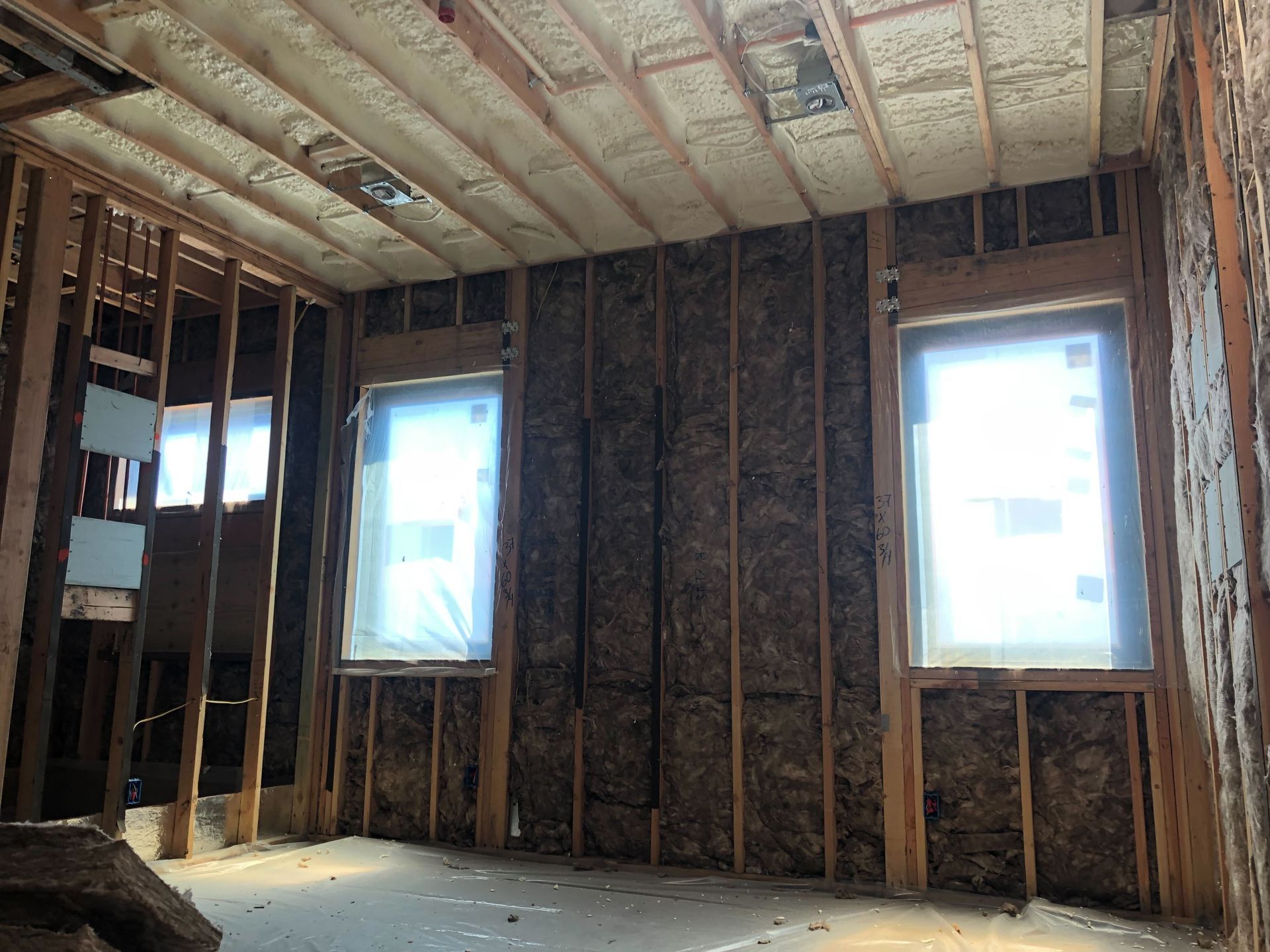Exposed framing and insulation in an unfinished room with two bright windows and a bare floor.