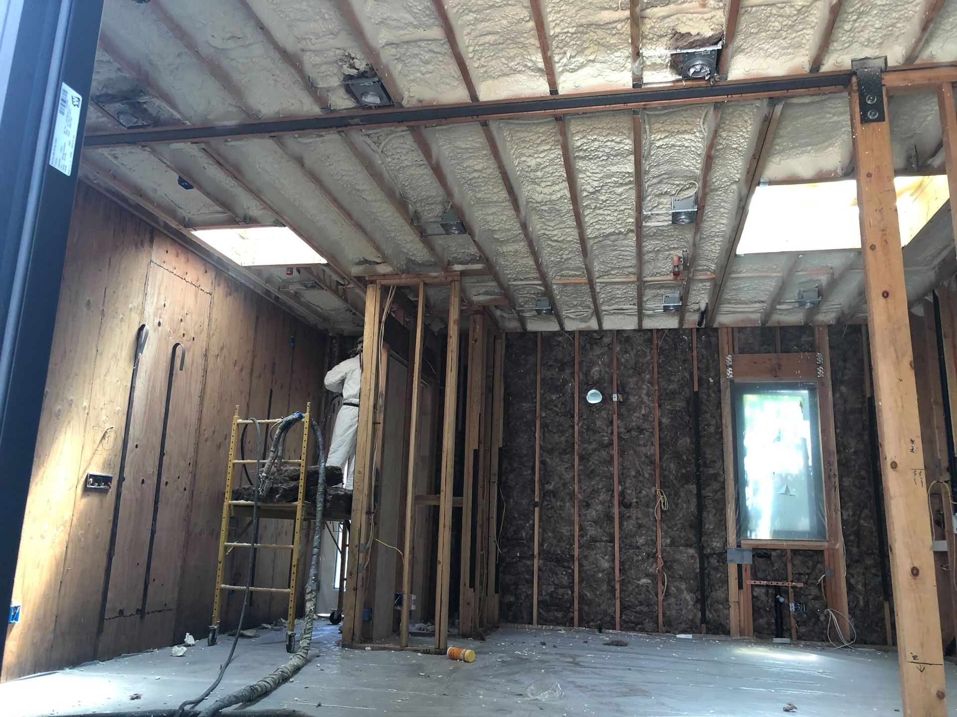 Interior under renovation with exposed studs, insulation, a ladder, and a window.