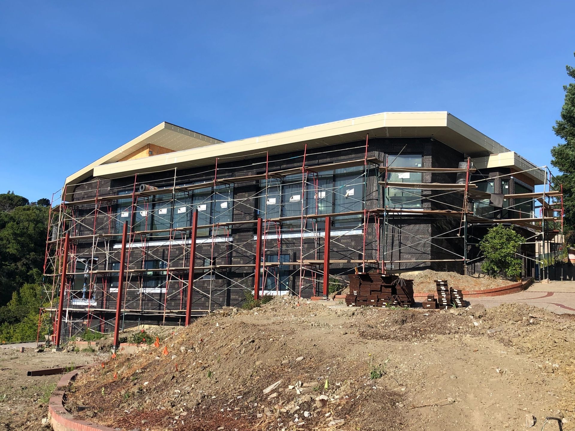 Building under construction with scaffolding on a dirt lot under a clear blue sky