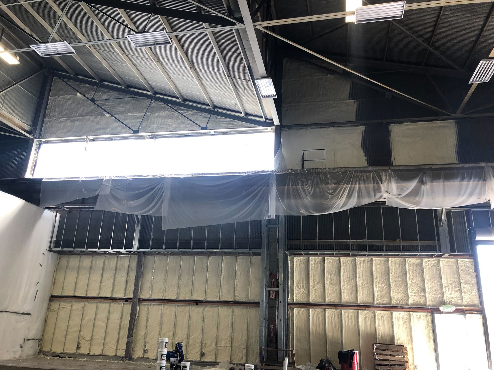 Interior of a warehouse with a high metal ceiling, bright skylight, and stacked insulated wall panels.
