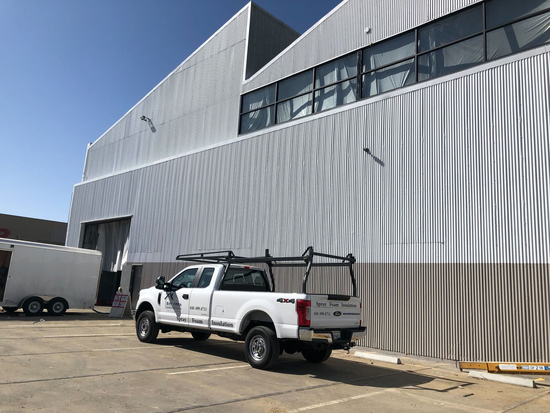 White pickup truck beside a corrugated metal building under a clear blue sky