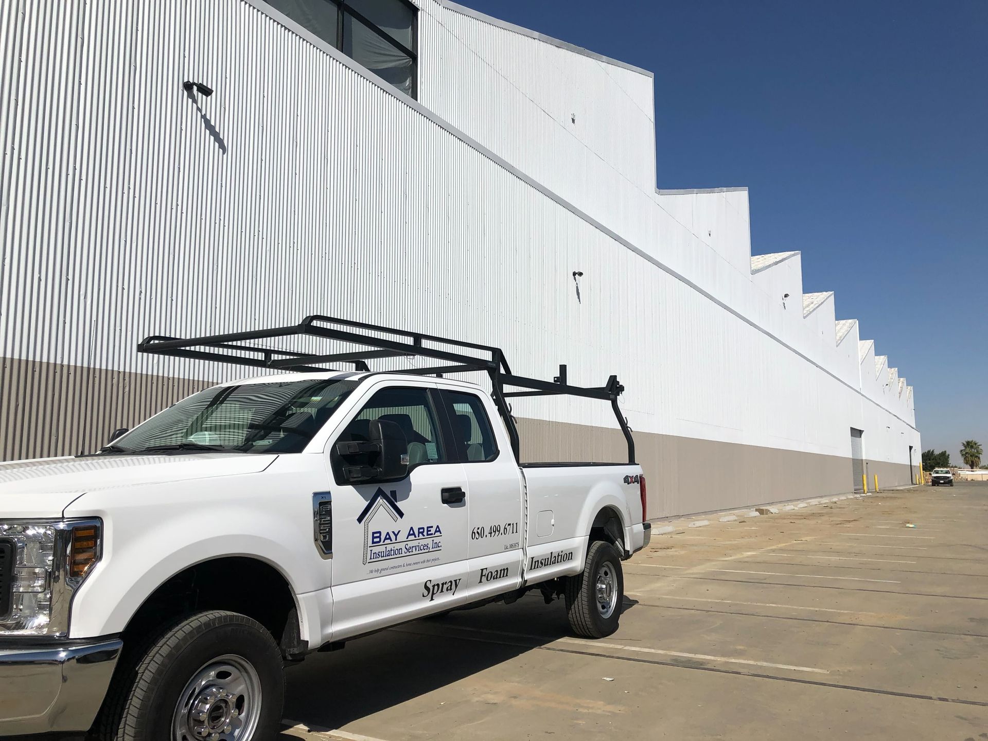 White utility truck parked beside a large white industrial building under a clear blue sky