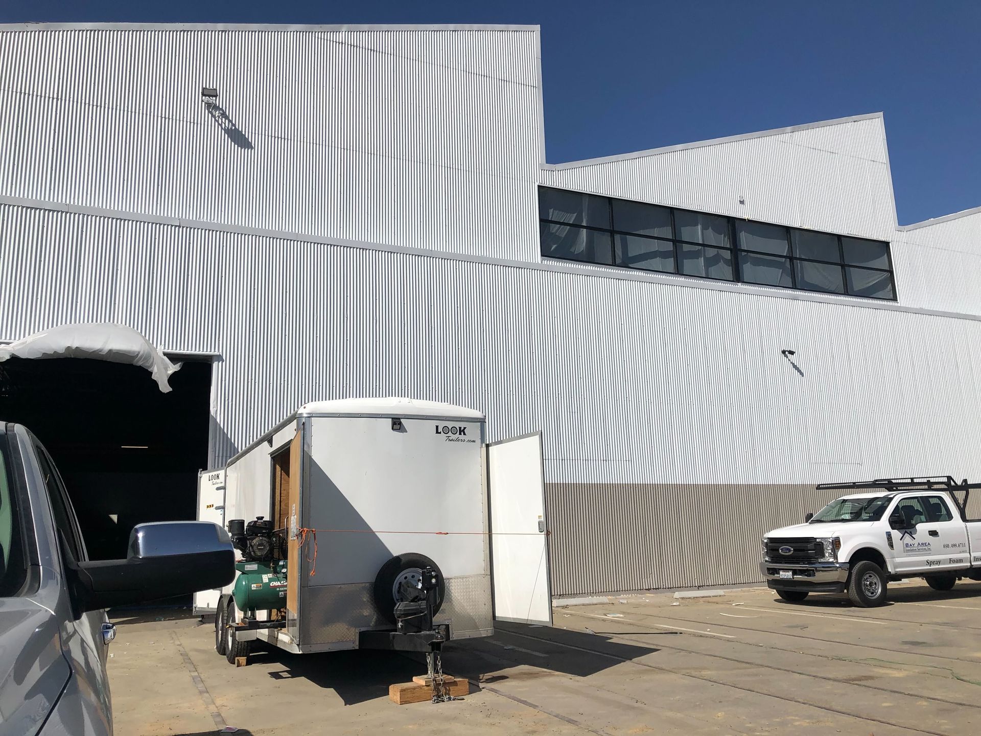 White industrial building with striped facade, loading dock, and parked truck and SUV in front